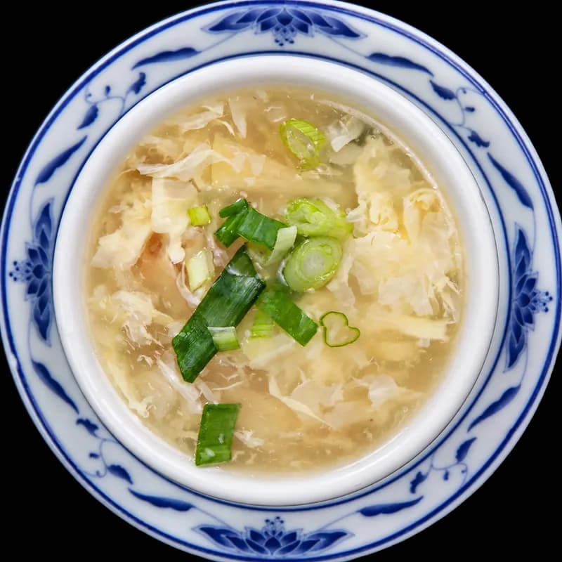 Egg drop soup with green onions in a blue and white bowl