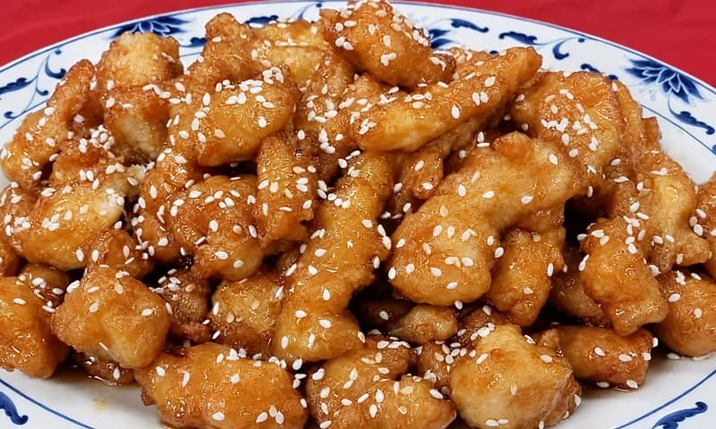 Sesame chicken with sesame seeds on a blue and white plate